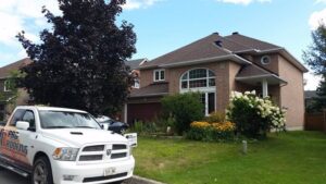 roofing project complete, brown roof brick house and green grass with A1 Pro Roofing truck parked in the street - A1 Pro Roofing Ottawa Kanata Orleans